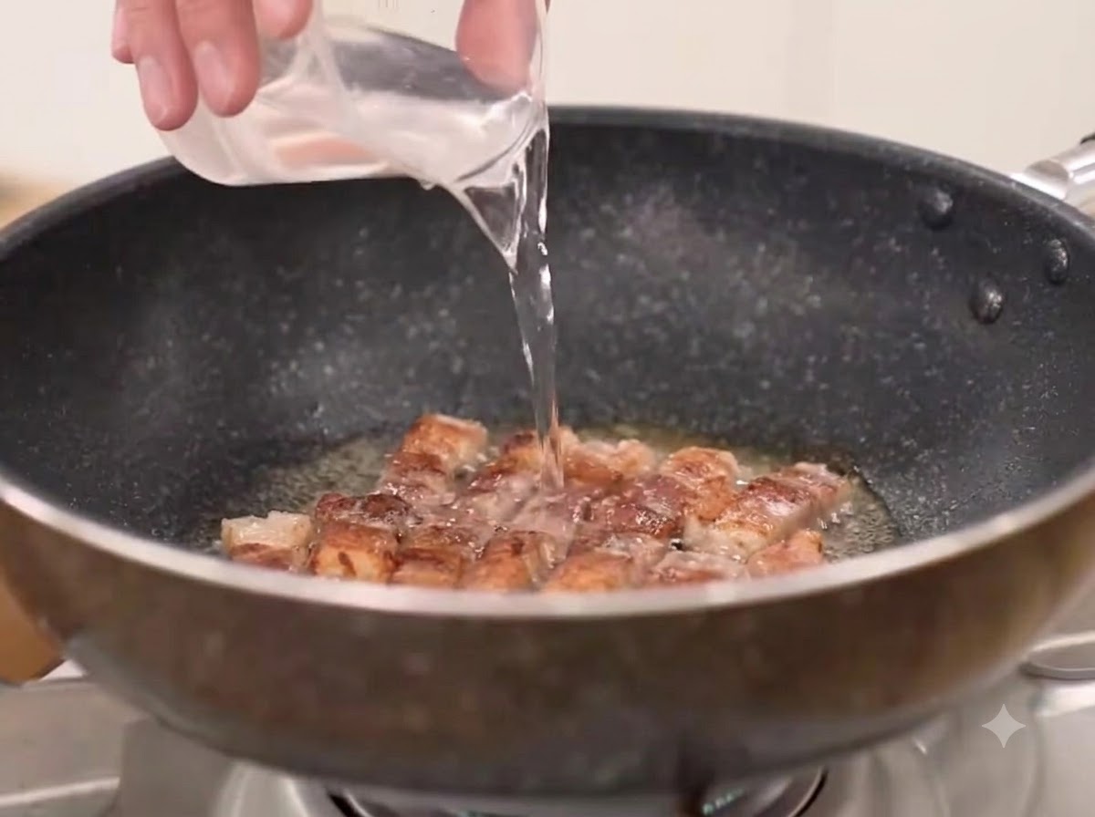 Water, coarse chili powder, and kimchi being added to the pan with the fried pork belly.