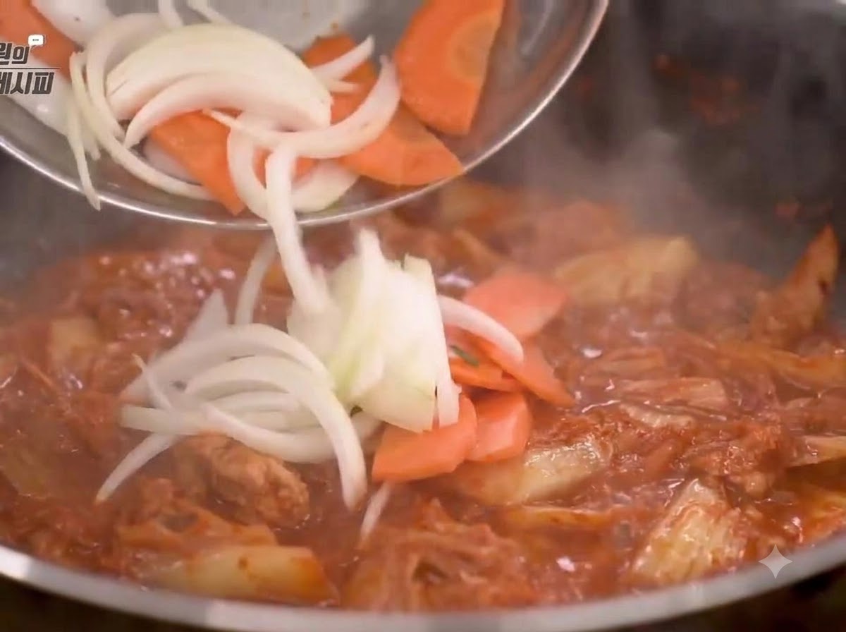 Cut onions and carrots being added to the pan and stir-fry with the kimchi mixture.