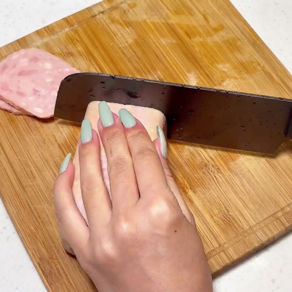 Luncheon meat being sliced uniformly on a wooden board with a knife.