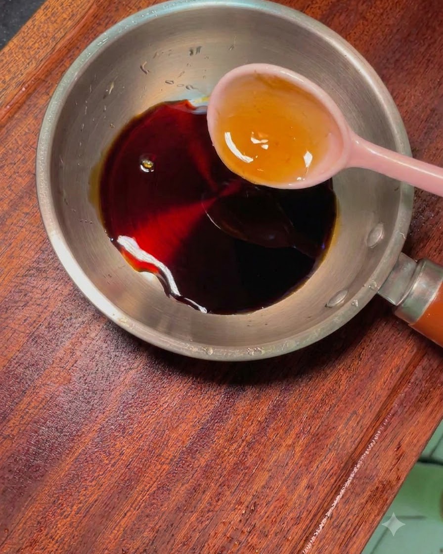 A small metal pan containing dark sauce and other seasonings, with a pink spoon resting inside.