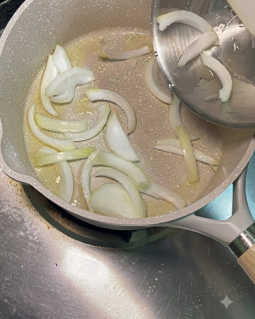 Sliced white onions being poured from a stainless steel bowl into a heated pan with cooking oil.