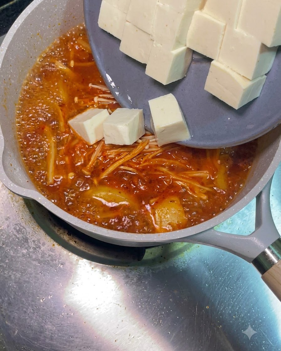 White tofu cubes sliding off a grey plate into the bubbling red soup.