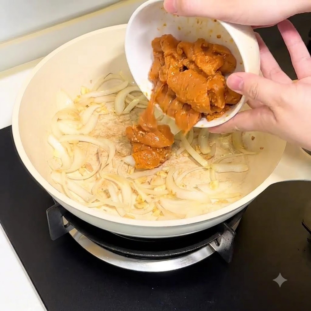 Chicken breast pieces being poured from a white bowl into the pan with onions and garlic.
