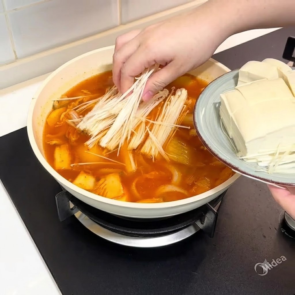 Enoki mushrooms and sliced tofu being added into the pot of broth.