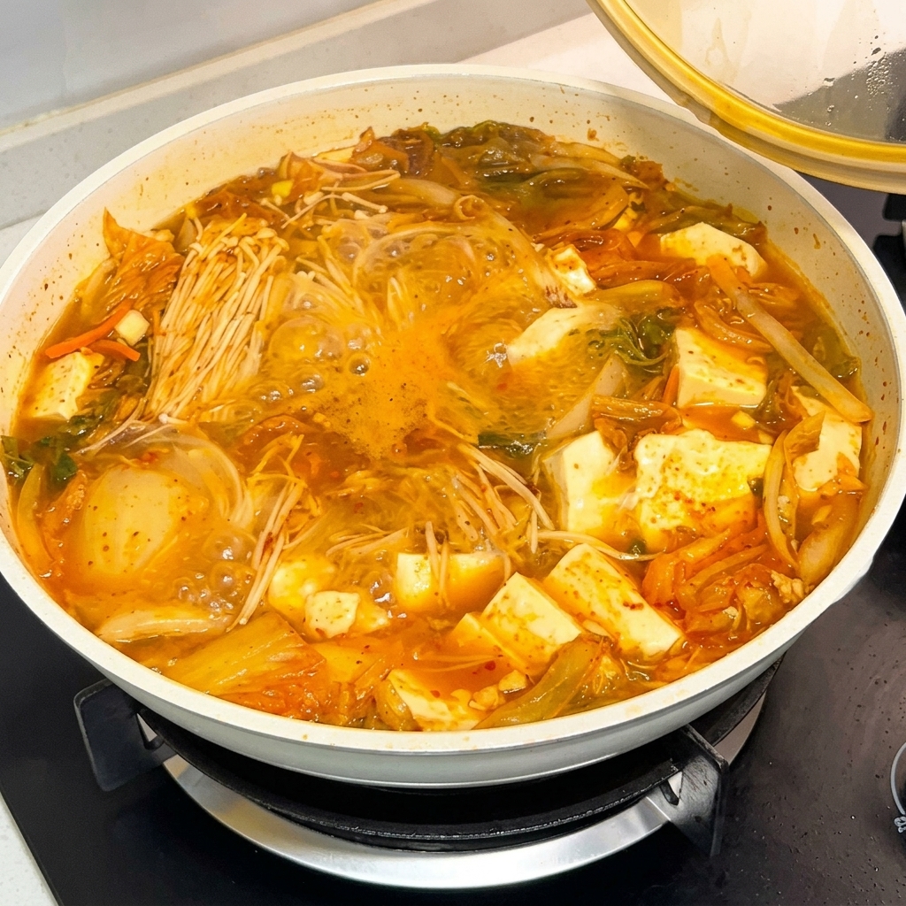 A spoonful of Korean chili paste sauce being poured into a bubbling pot of soup.