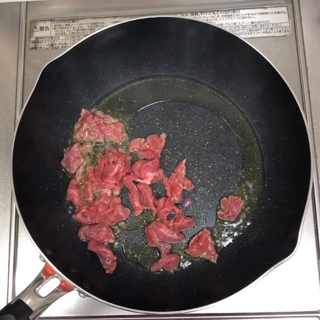 Beef slices sizzling and browning in a hot oiled pan.