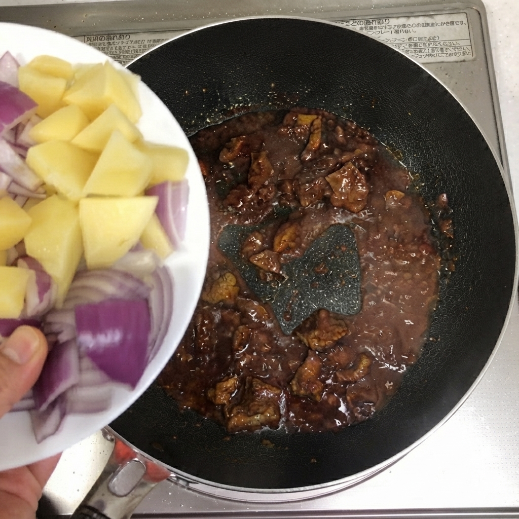 Sliced potatoes and red onions being poured into the pan with beef.