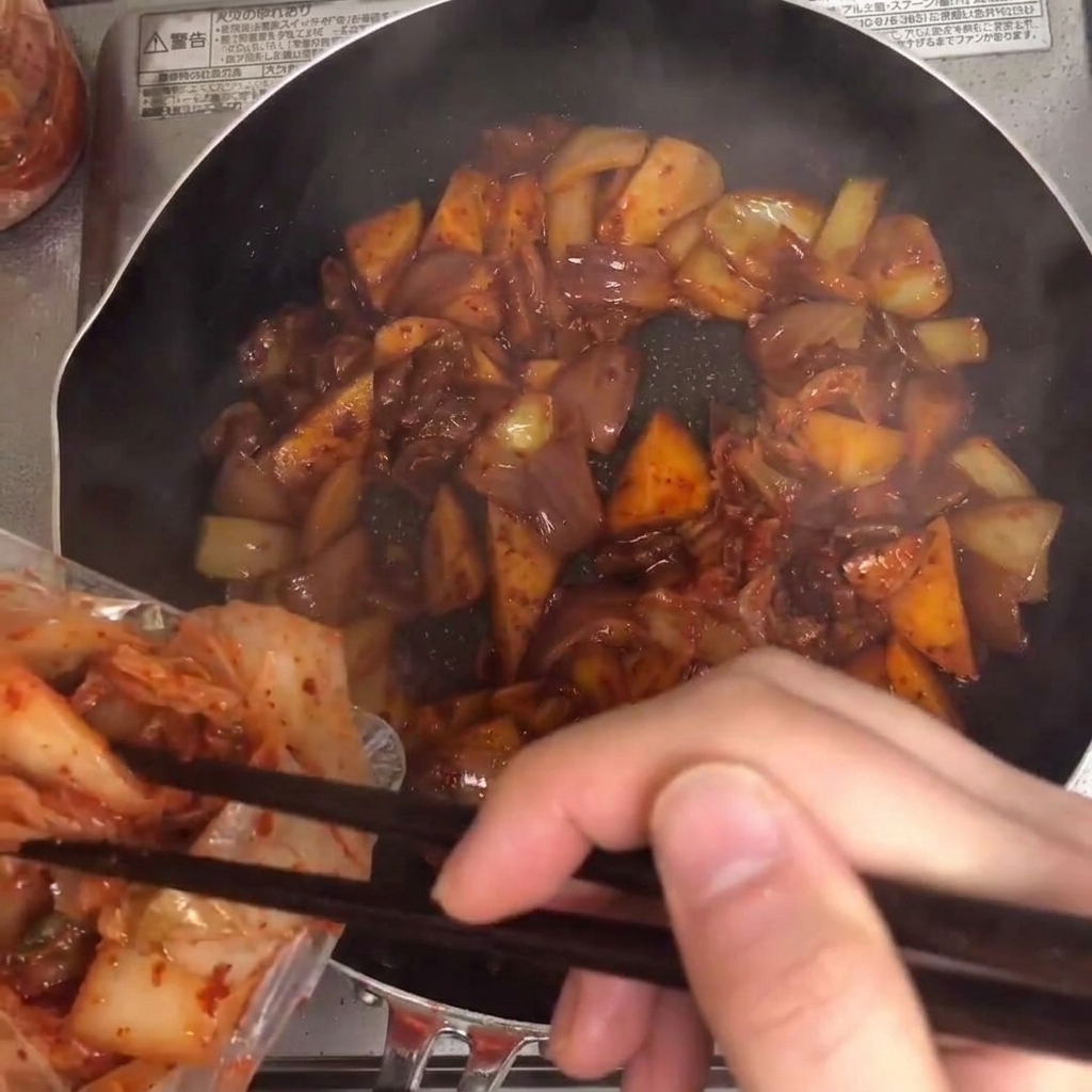 Kimchi being added to the pan and mixed with the other ingredients.