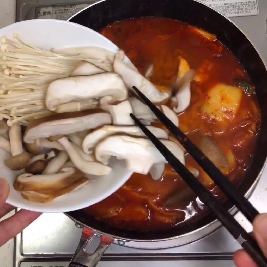 Assorted mushrooms and enoki mushrooms being placed into the simmering soup pot.