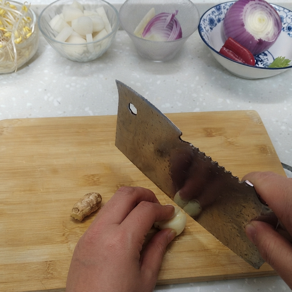 Garlic cloves and fresh ginger root being sliced on a cutting board next to bowls of ingredients.