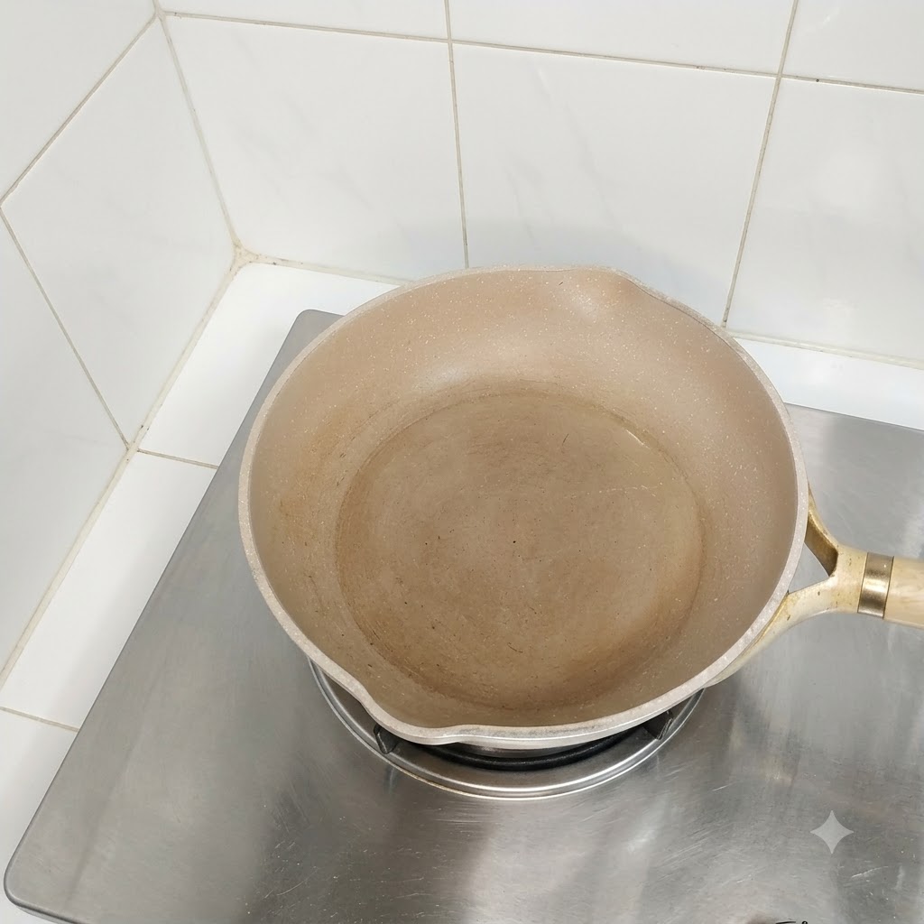 An empty oiled pan sitting on a stovetop burner ready for cooking.