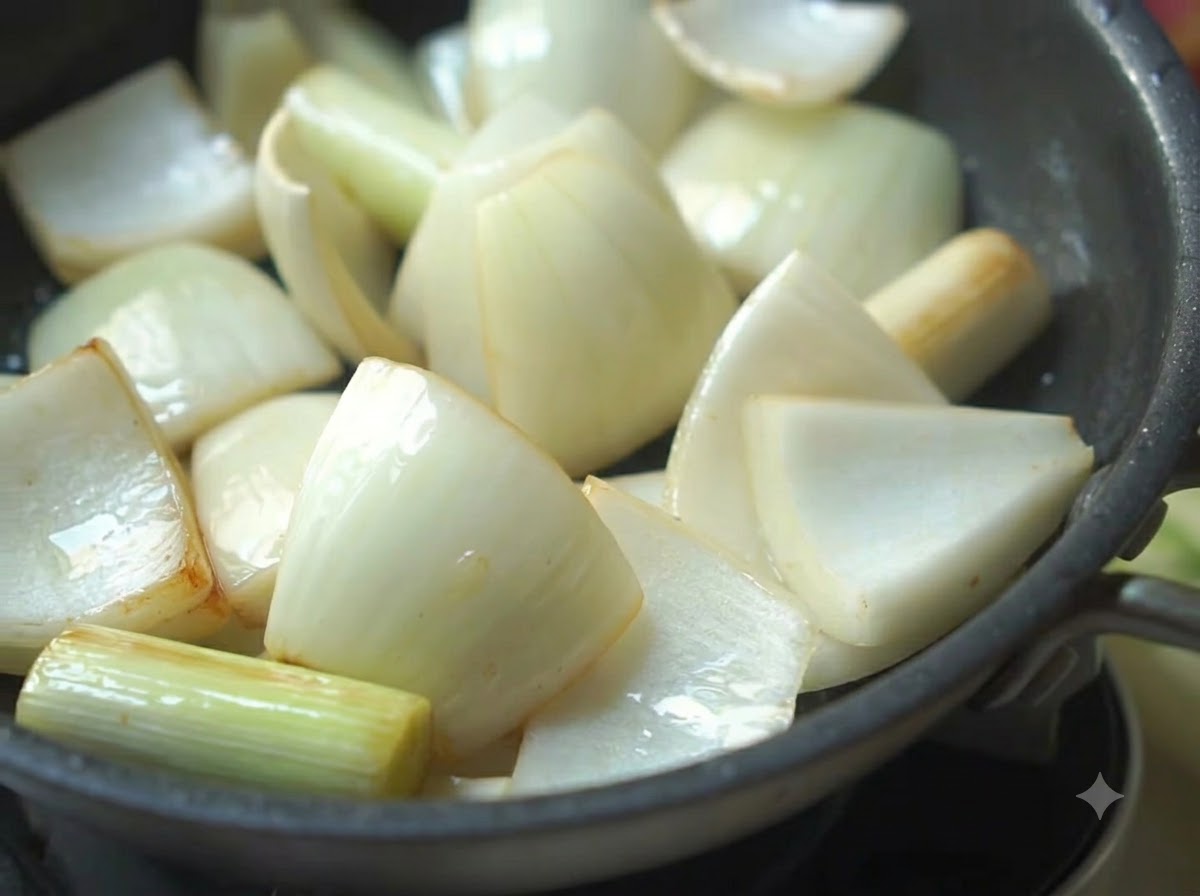 Onions, scallions, and green peppers sizzling in a frying pan with oil.