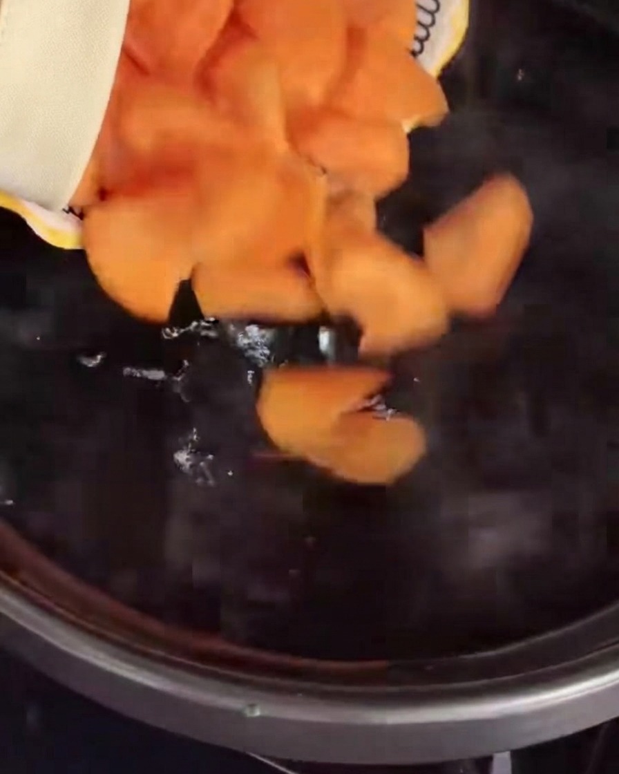 Sliced carrots being poured into a pot of boiling water.