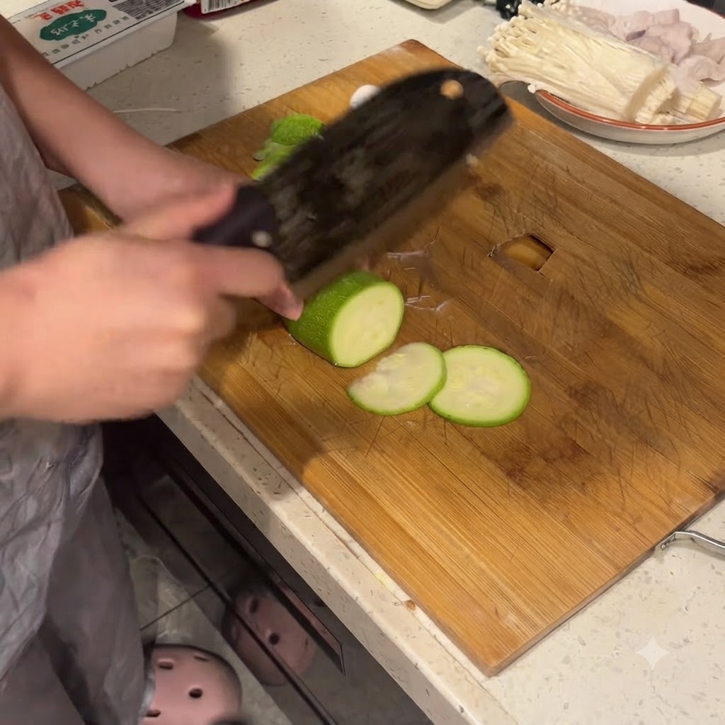 Zucchini being cut into neat rounds on a wooden cutting board with a large cleaver.