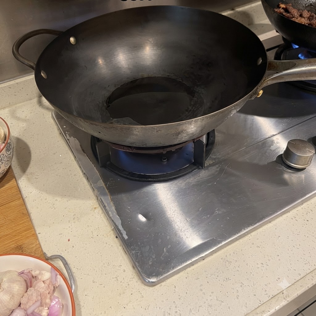 Pork belly and red onion sizzling in a hot wok with oil.
