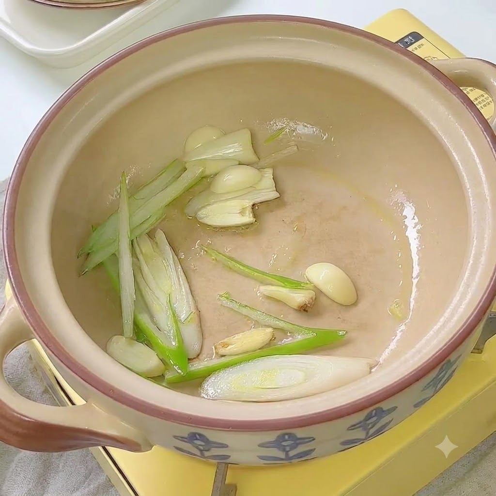 Kimchi being stir-fried with scallions and garlic inside a ceramic pot.
