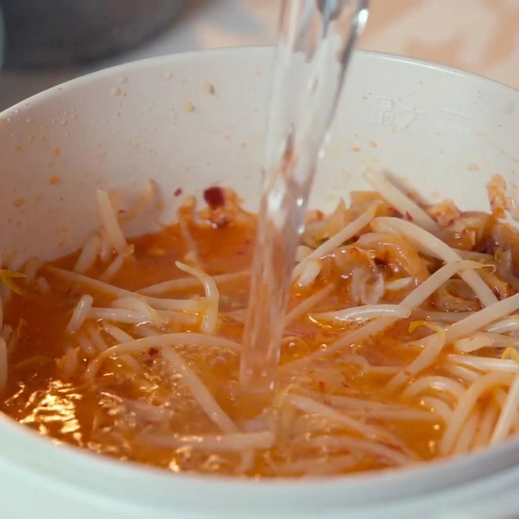 Water being poured from above into the pot containing kimchi and bean sprouts.