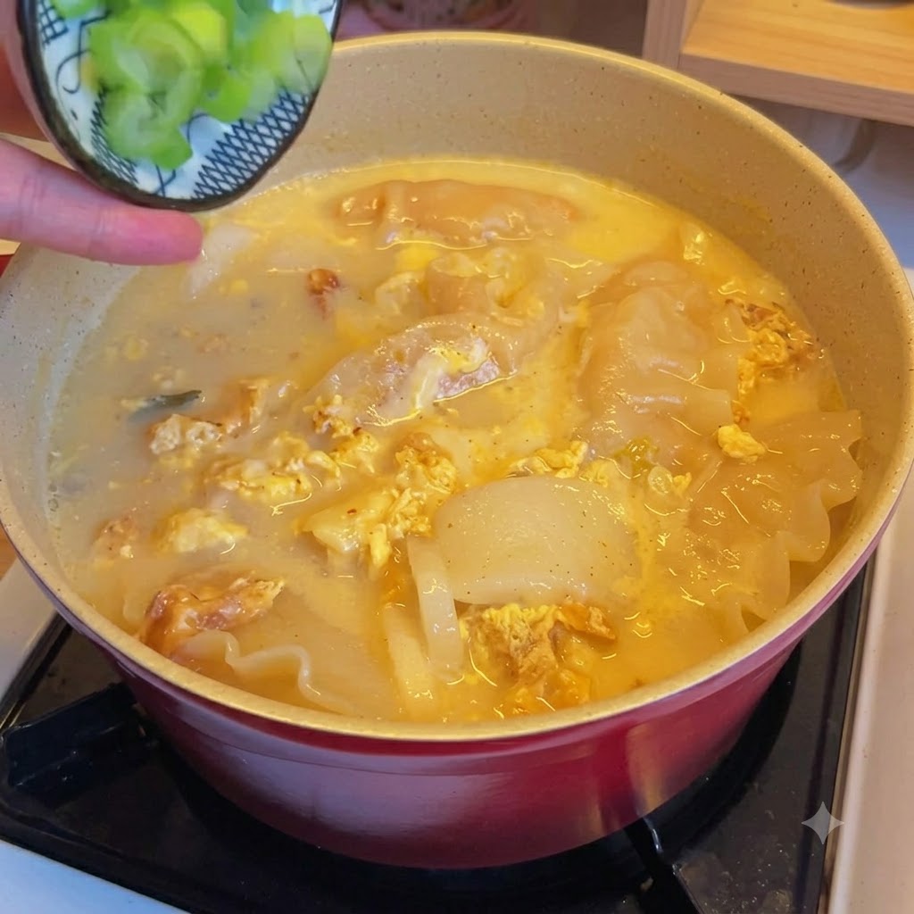 Chopped green onions being sprinkled over a pot of kimchi dumpling soup.