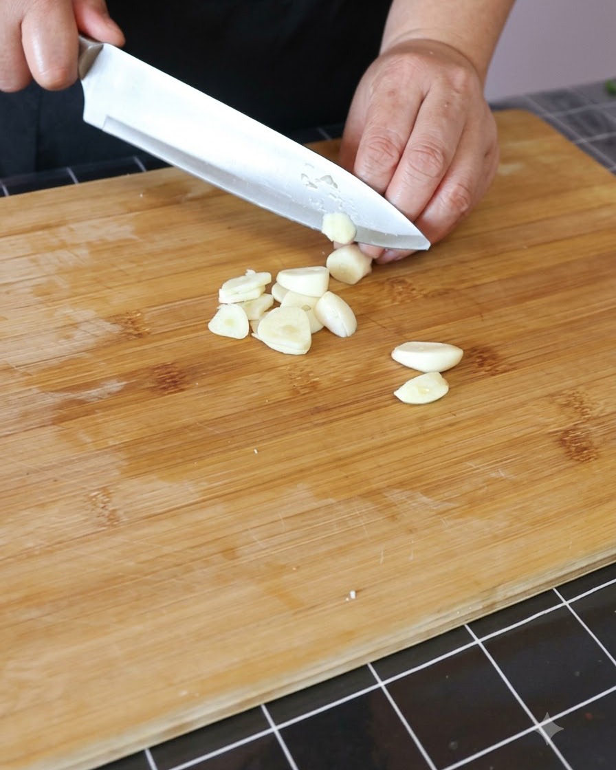 Garlic cloves being minced on a wooden cutting board.
