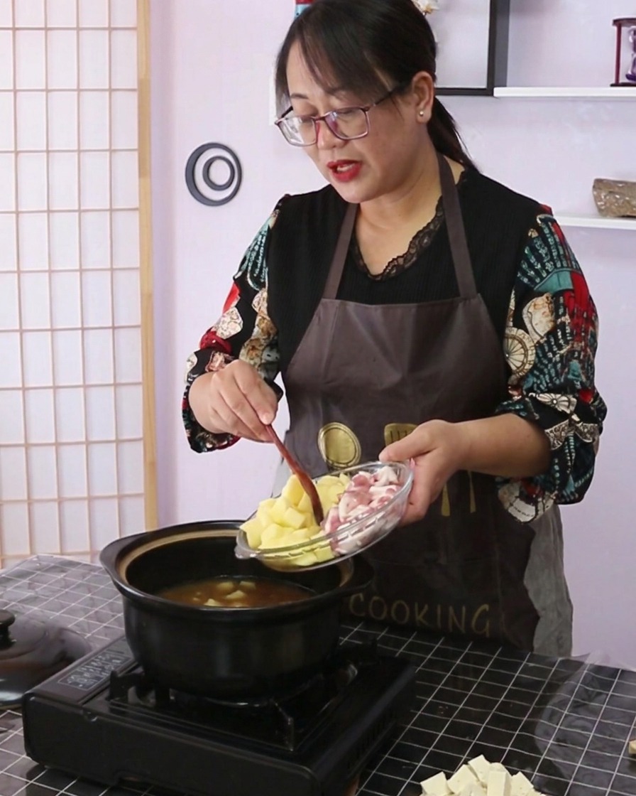 Diced potatoes and sliced pork belly being tipped from a glass dish into the cooking pot.