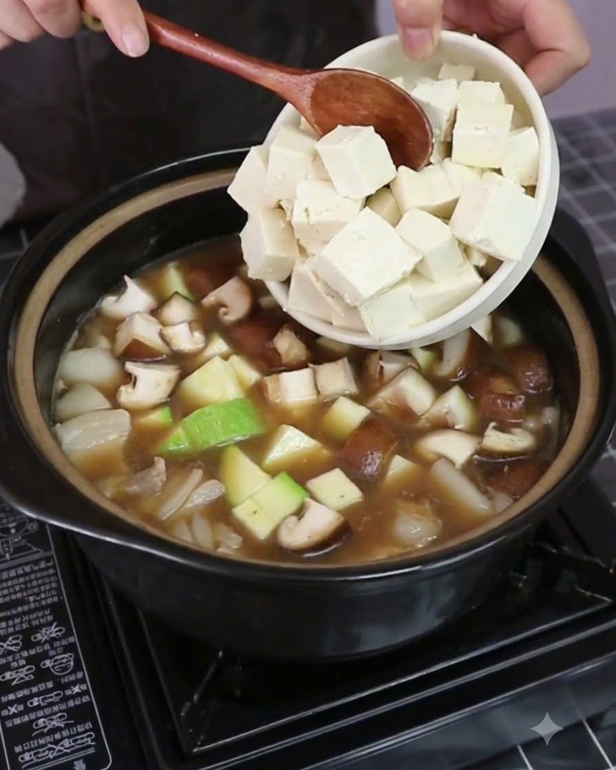 Brine firm tofu cubes being added into the pot with vegetables and broth.