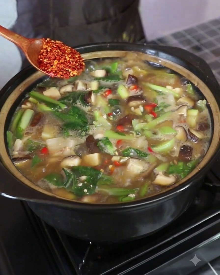 A wooden spoon holding red chili flakes over the boiling soup pot while being stirred.