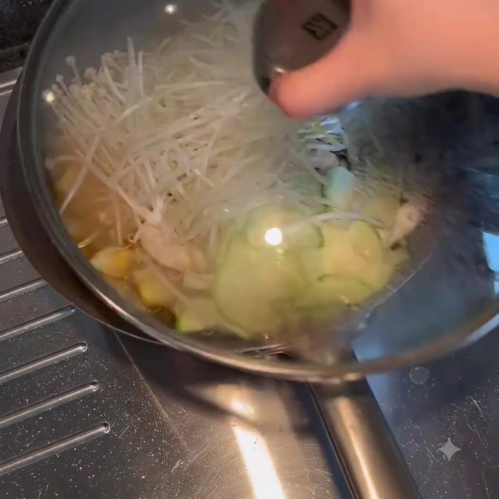 A glass lid being placed over a frying pan filled with simmering vegetables and broth.