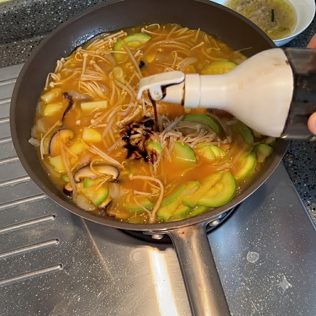 Soy sauce being squeezed from a bottle into the simmering vegetable stew.