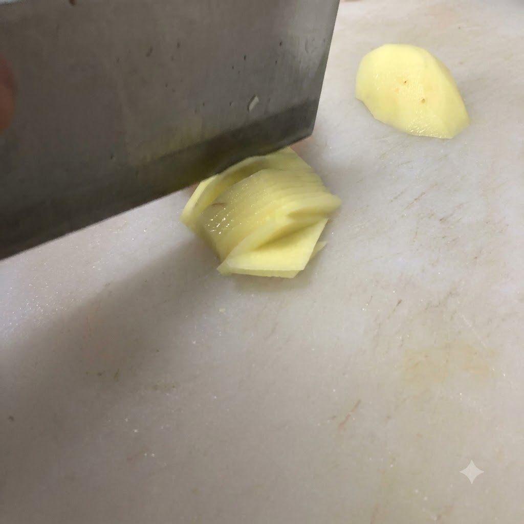 A knife slicing a potato into thin pieces on a white cutting board.