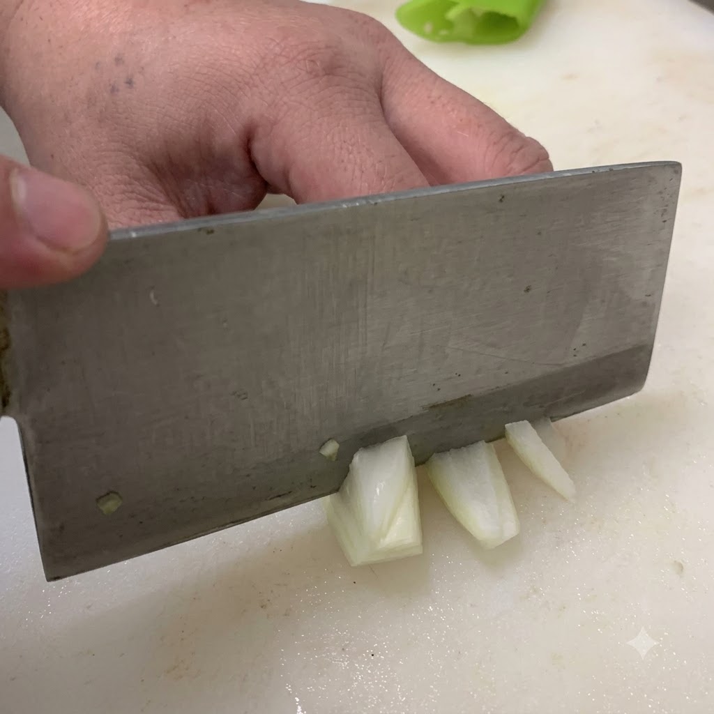 A knife cutting an onion into chunks on a white cutting board.