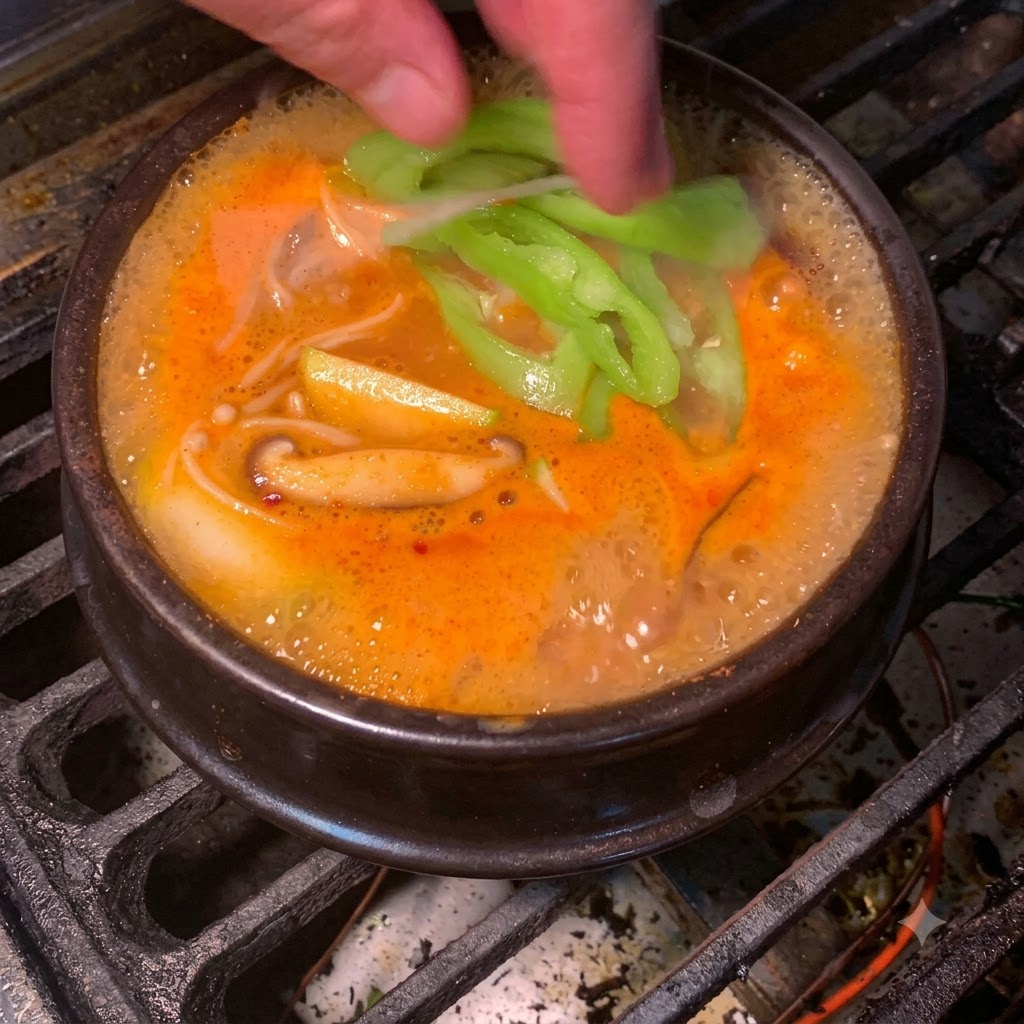 Fresh green chili slices being dropped into the bubbling orange-red Korean soybean paste stew.