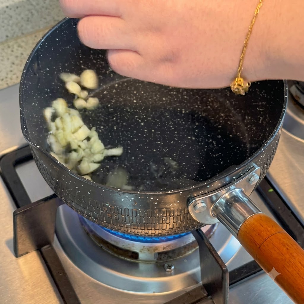 Sliced garlic sizzling in hot oil inside a pot on a gas burner.