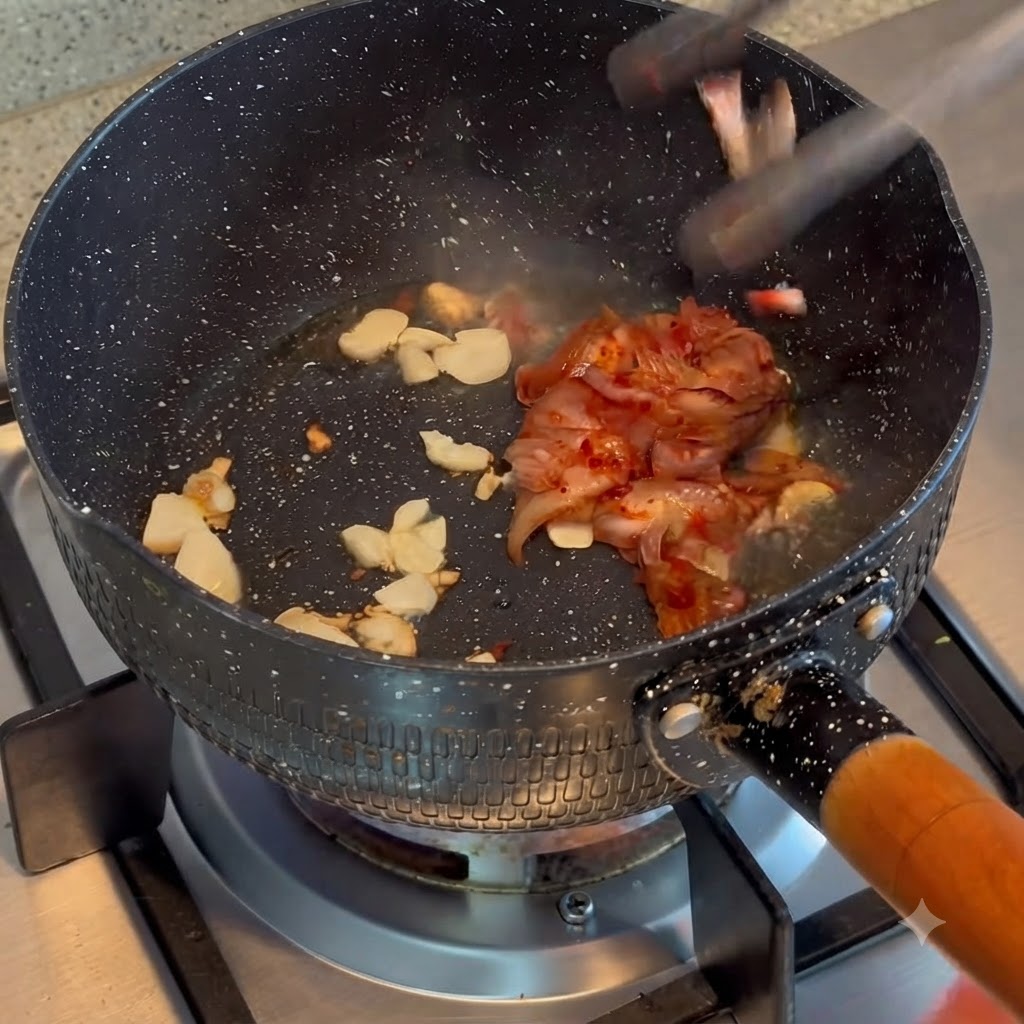 Kimchi being tossed and stir-fried with fried garlic in a cooking pot.