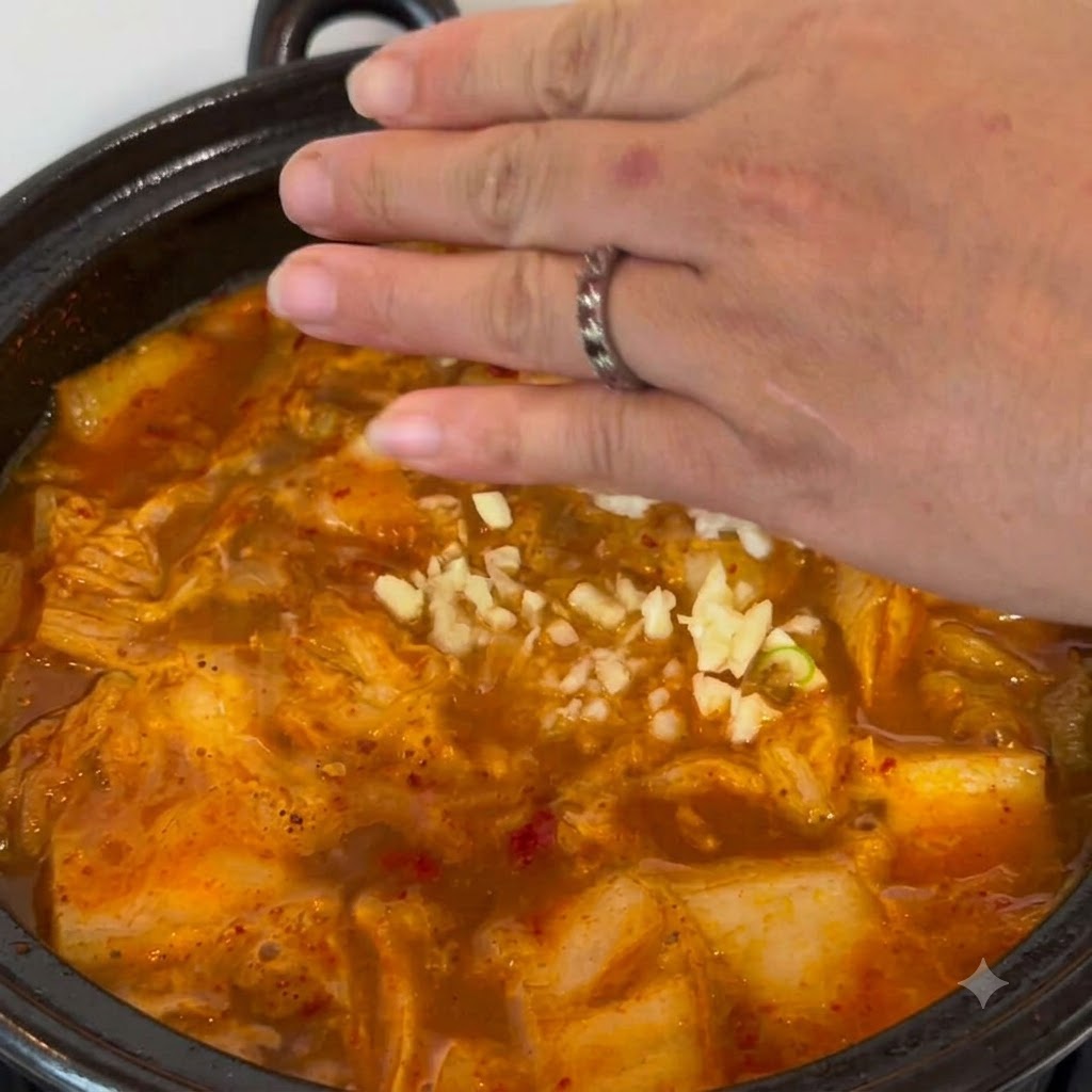 Minced garlic being sprinkled by hand into the bubbling stew pot.