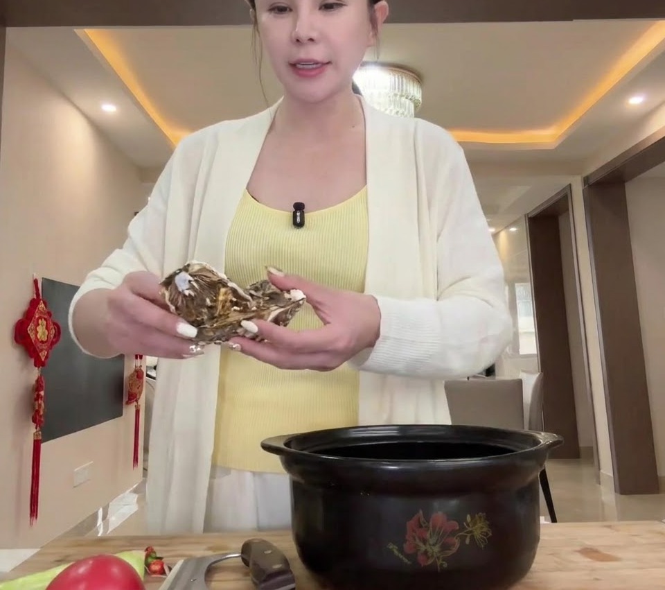 Raw oysters being placed at the bottom of a large black clay pot.