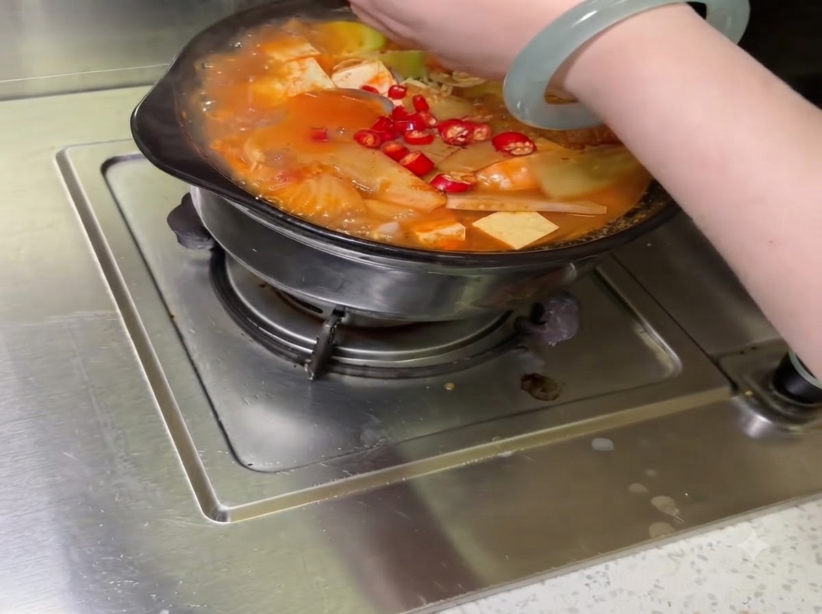 Assorted sliced vegetables and chili peppers being arranged inside the cooking pot.