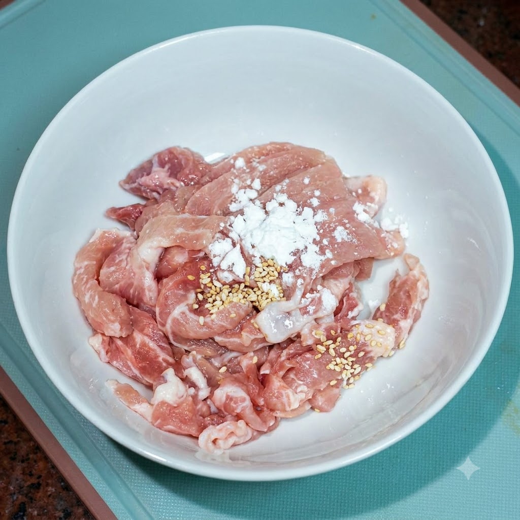 Sliced pork in a white bowl being seasoned with a little chicken bouillon and cooking oil.