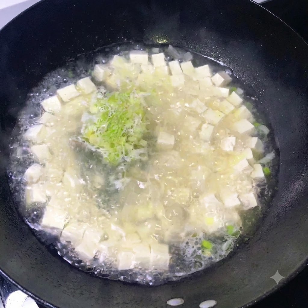 Seasonings being sprinkled over a bubbling pot of tofu and chopped green onions.