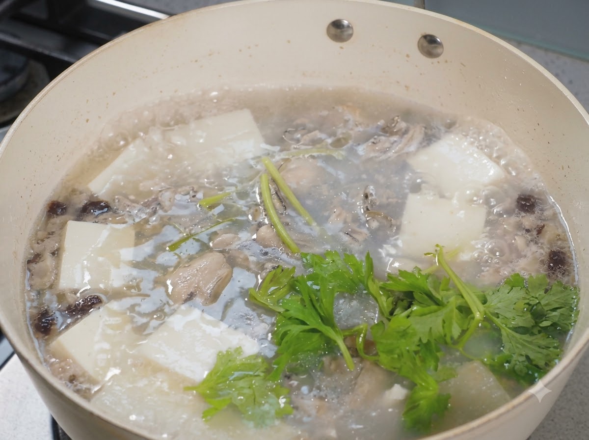 Fresh celery leaves scattered over a bubbling pot of oyster and tofu soup.