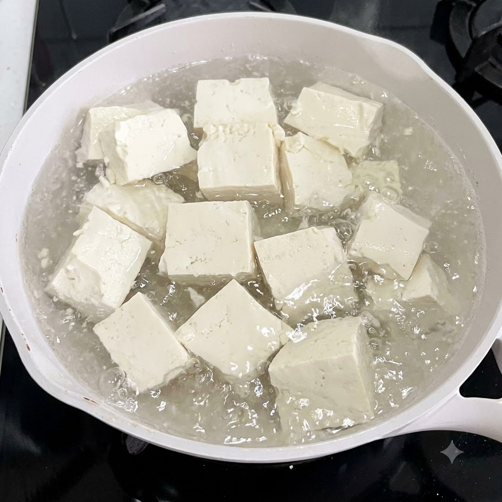 Tofu cubes boiling in a white pot of water with ginger slices.
