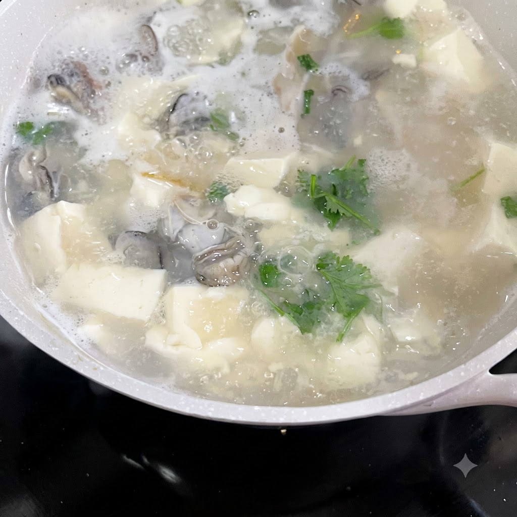Chopped cilantro and green onions being added to a bubbling pot of oyster and tofu soup.