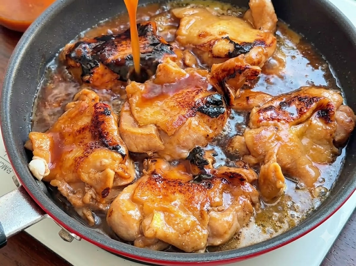 A stream of dark brown sauce being poured from above into a pan filled with browned chicken thighs.