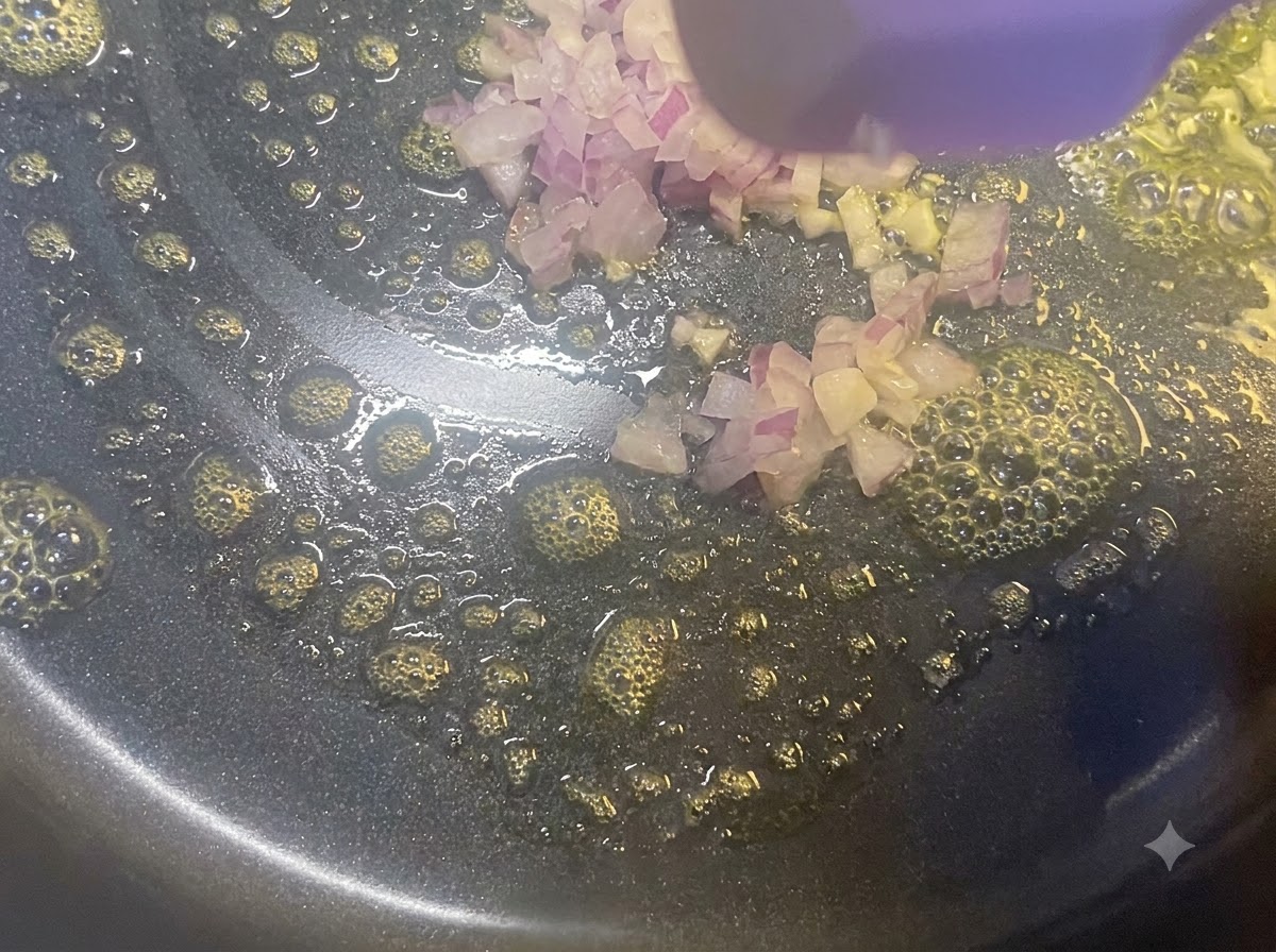 Diced red onions being sautéed in a frying pan with melted butter using a wooden spatula.