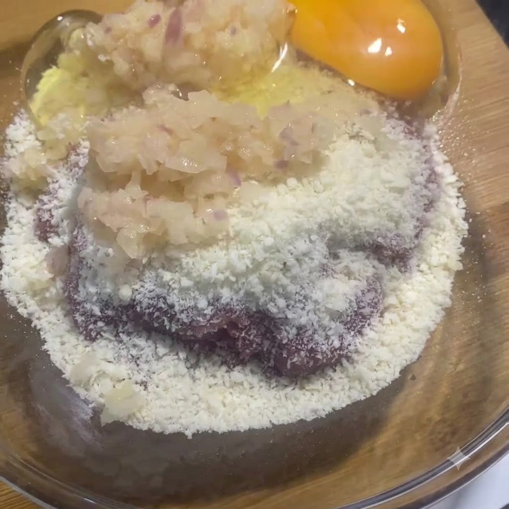 A raw egg yolk and white sitting in the glass bowl alongside the meat and onion mixture.