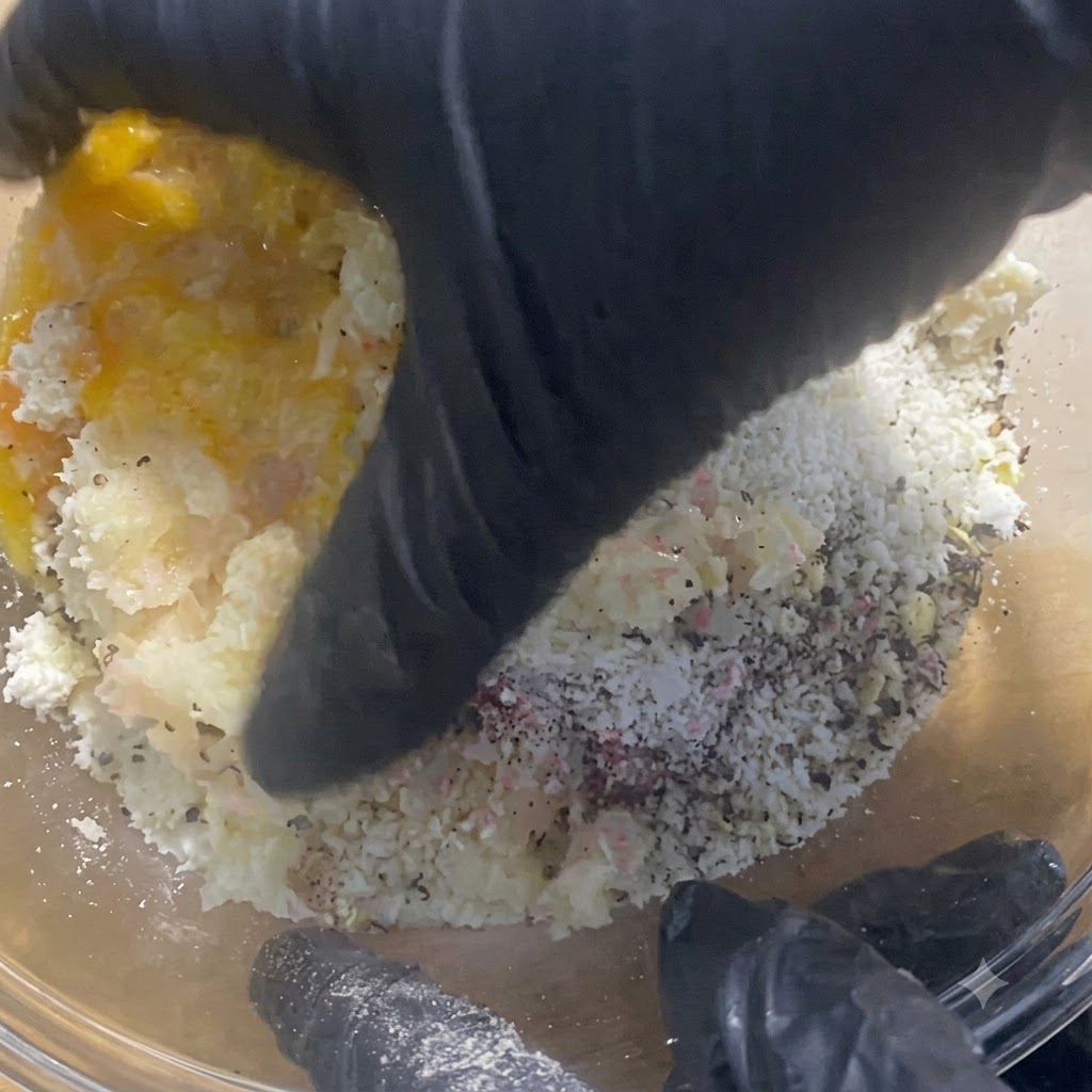 Gloved hands thoroughly mixing and kneading the meat filling inside the glass bowl.
