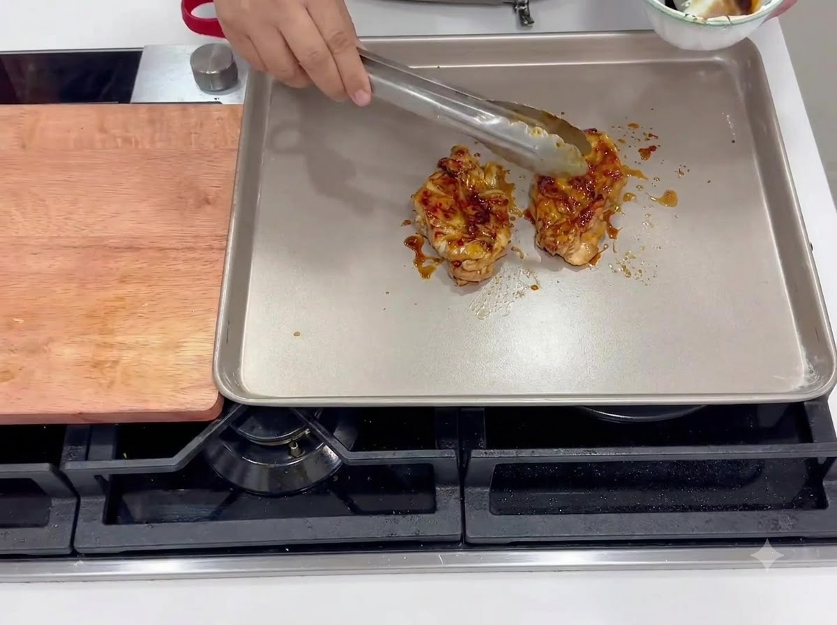 Marinated chicken thighs frying skin-side down in a heated square pan.