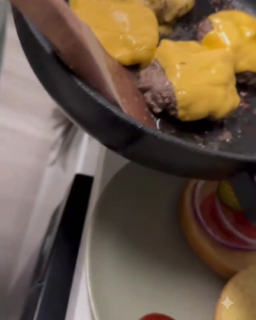 Yellow cheddar cheese melting on top of beef patties inside a skillet.