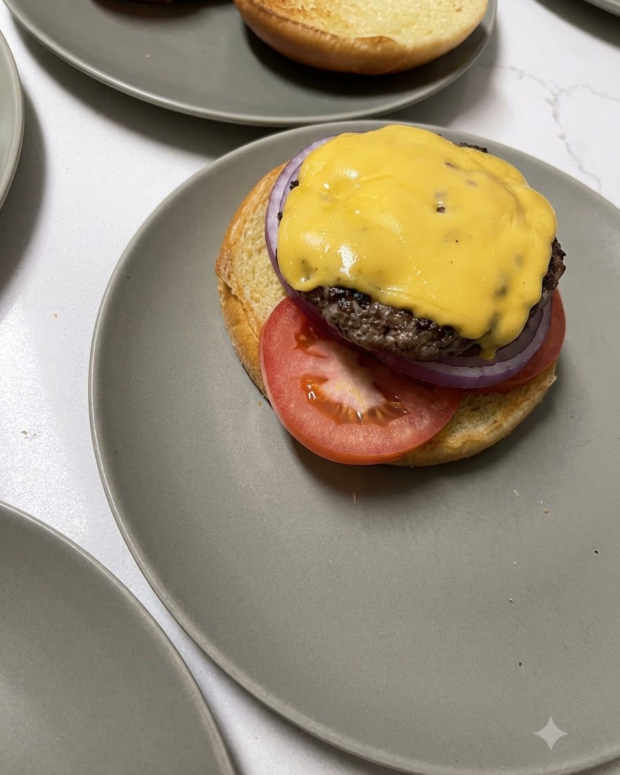 A cheese-topped beef patty being transferred from a wooden spatula onto a burger base.