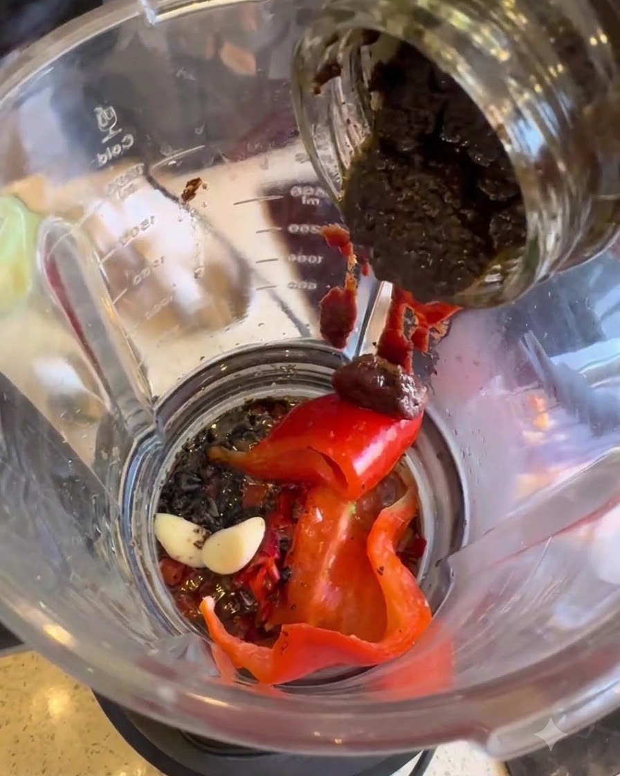 Black truffle paste being transferred from a jar into the blender.