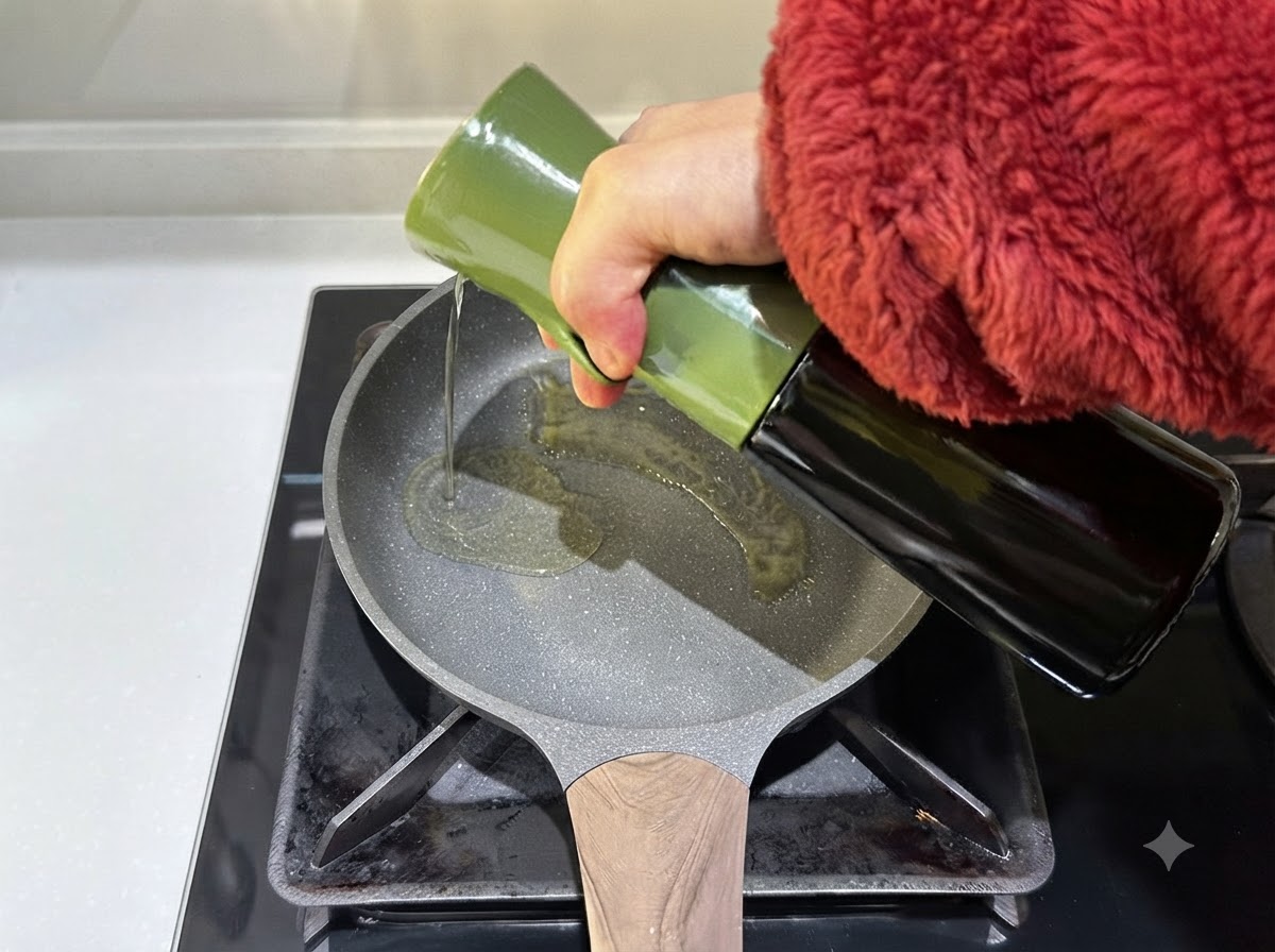 Olive oil being poured from a green container into a hot frying pan.